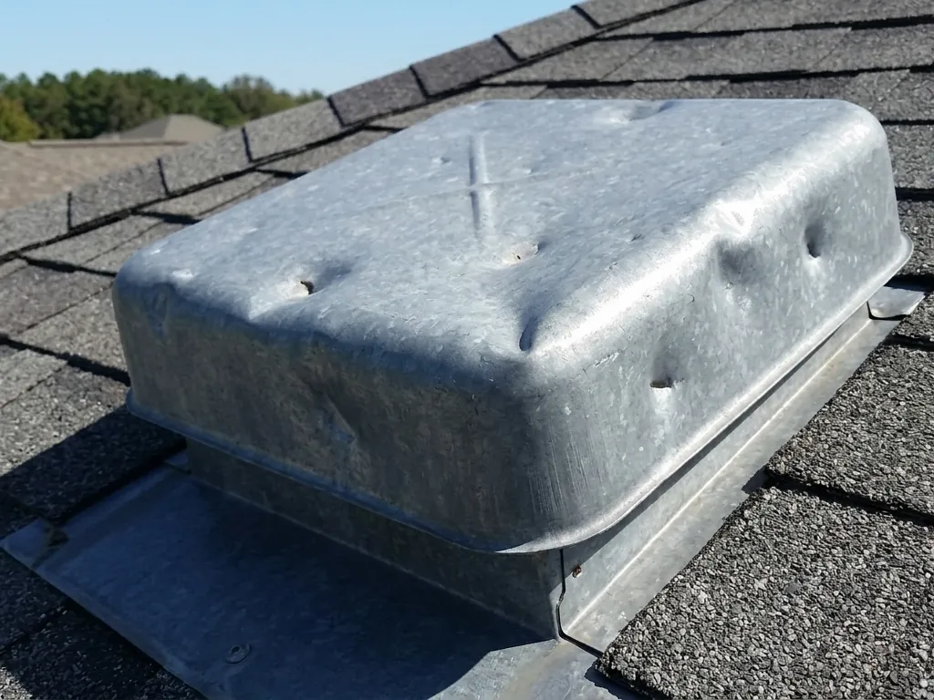 Galvanized metal roof vent cap covered in hail dents